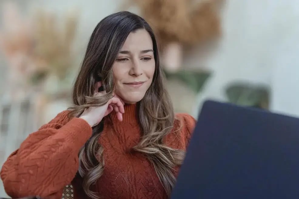 Smiling woman thinking and looking at a laptop